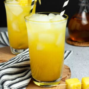 Two glasses of pineapple ginger beer mocktail with black and white striped straws.