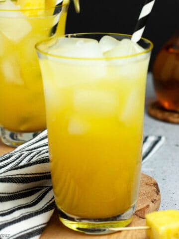 Two glasses of pineapple ginger beer mocktail with black and white striped straws.