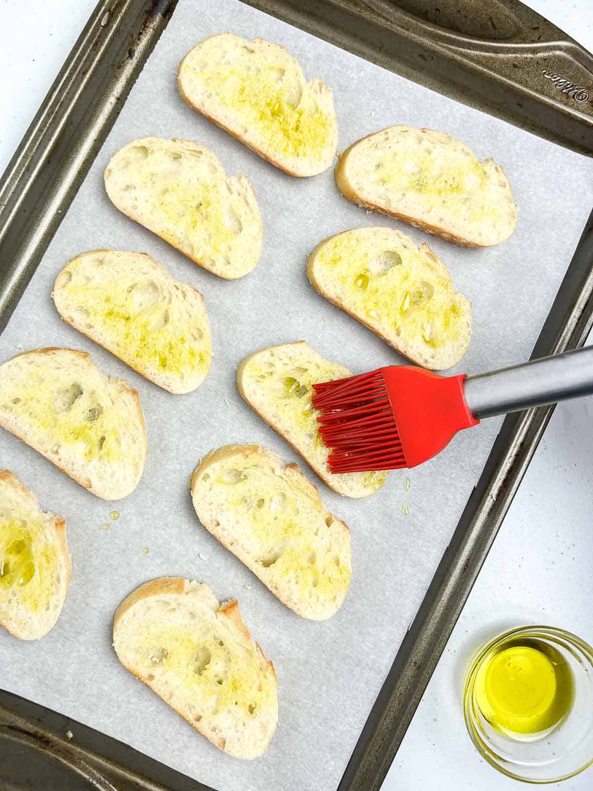Brushing baguette slices with olive oil before toasting to make crostini.