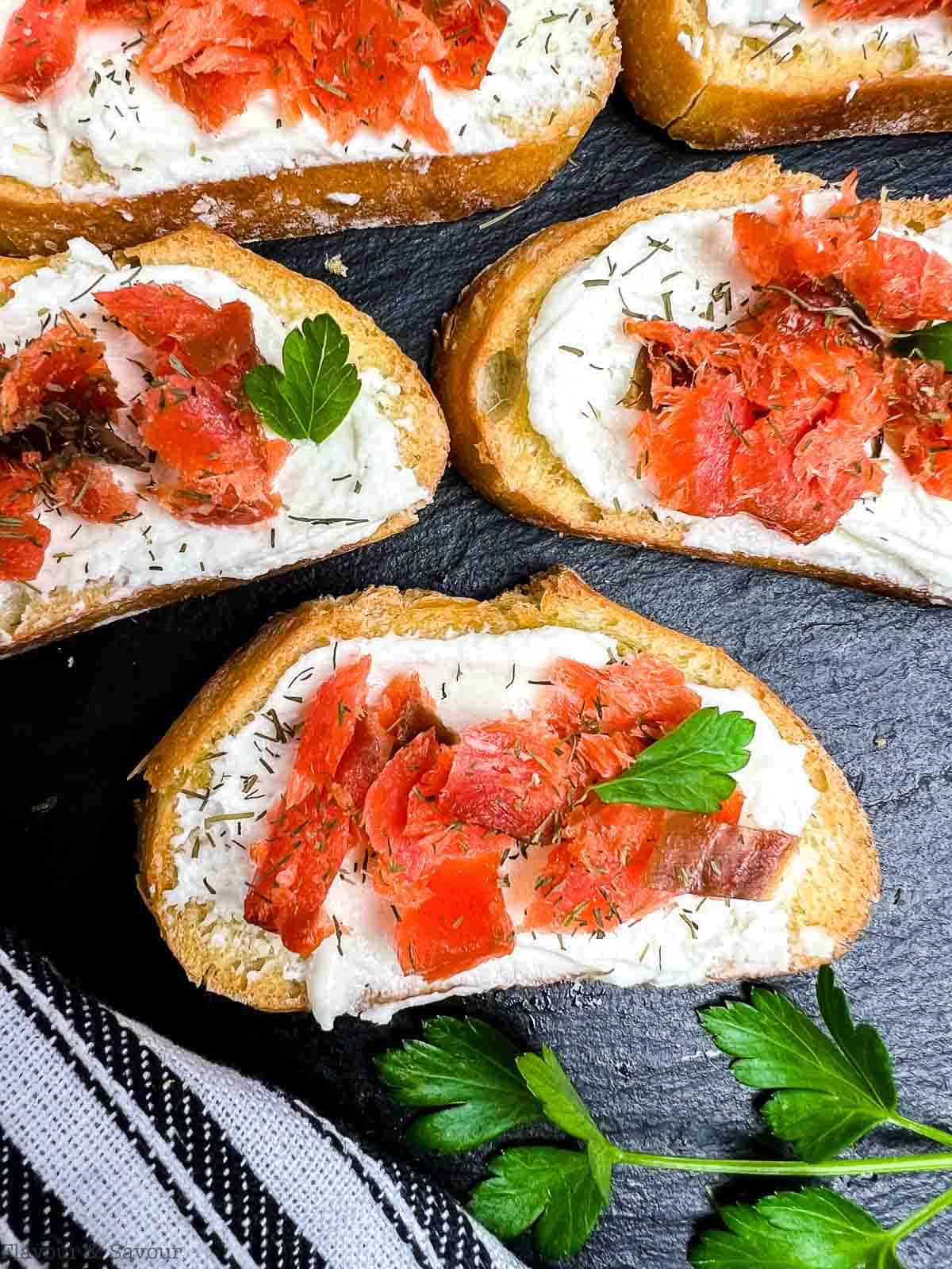 Overhead view of a black platter with smoked salmon crostini appetizers.