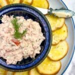A blue bowl filled with smoked salmon dip surrounded by crostini.