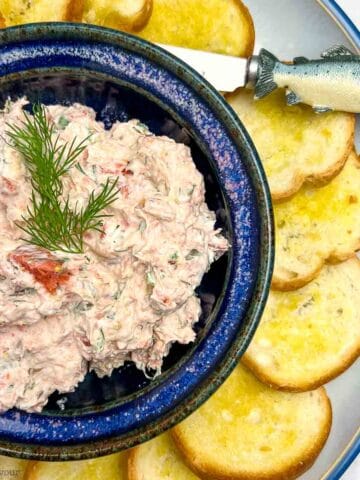 A blue bowl filled with smoked salmon dip surrounded by crostini.