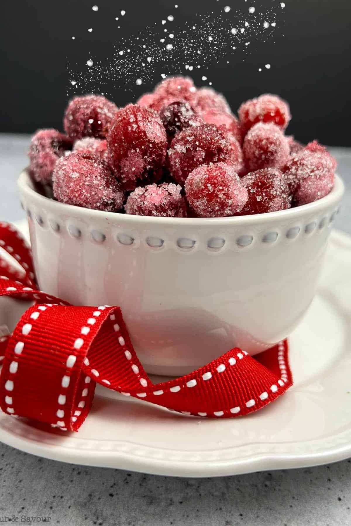 A bowl of sparkling sugared cranberries with a red ribbon.