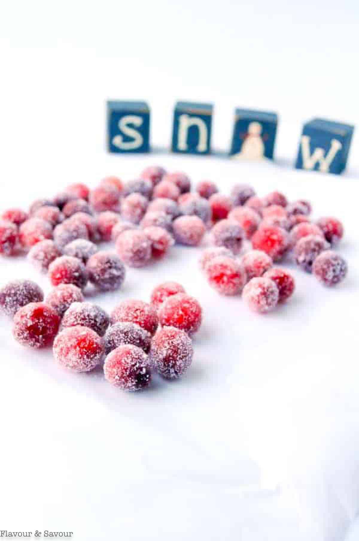 Sparkling sugared cranberries drying on a sheet of parchment paper.