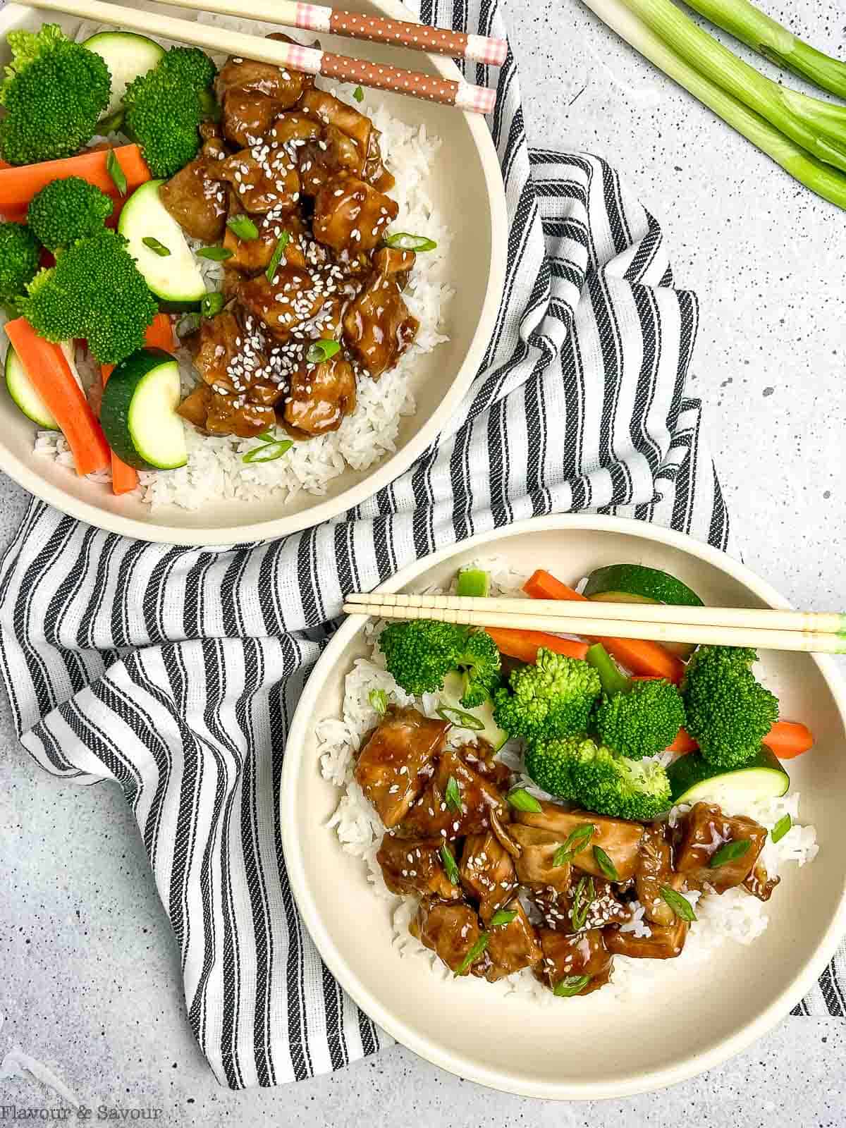 Overhead view of rice bowls with chicken, broccoli, zucchini, carrots and teriyaki sauce.