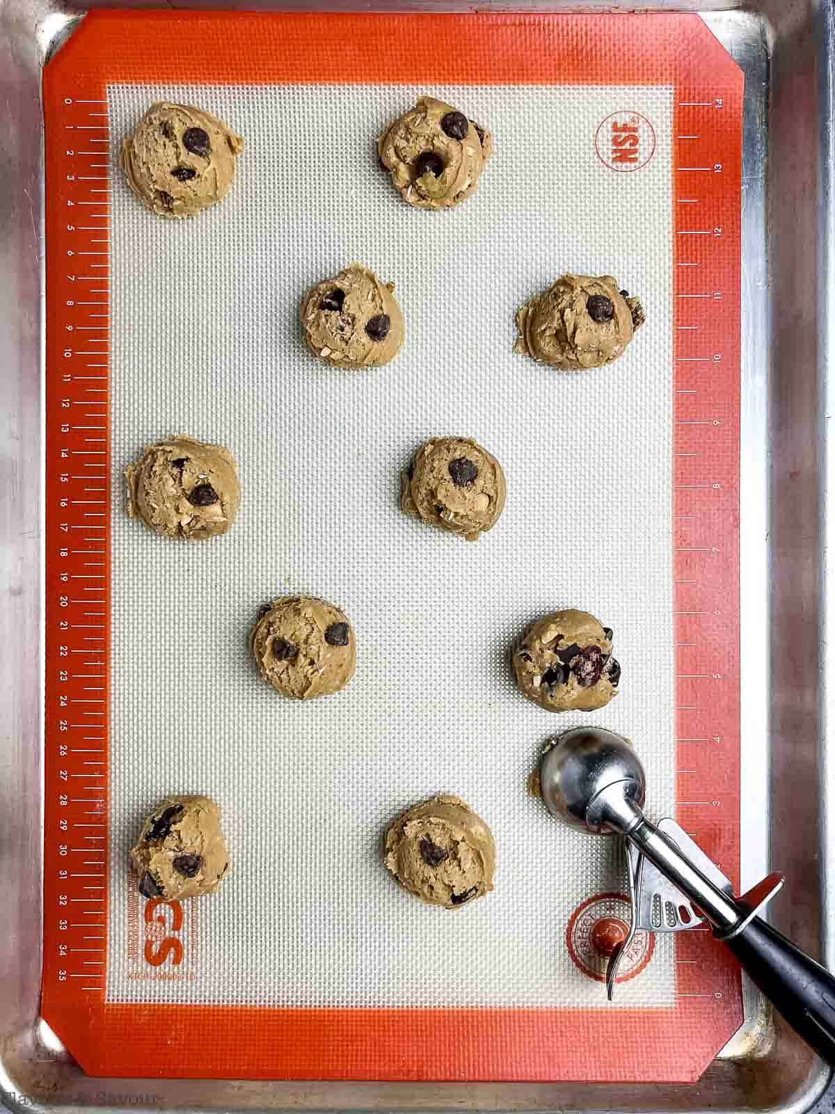 Balls of kitchen sink cookie dough on a silicone baking sheet with a cookie scoop.