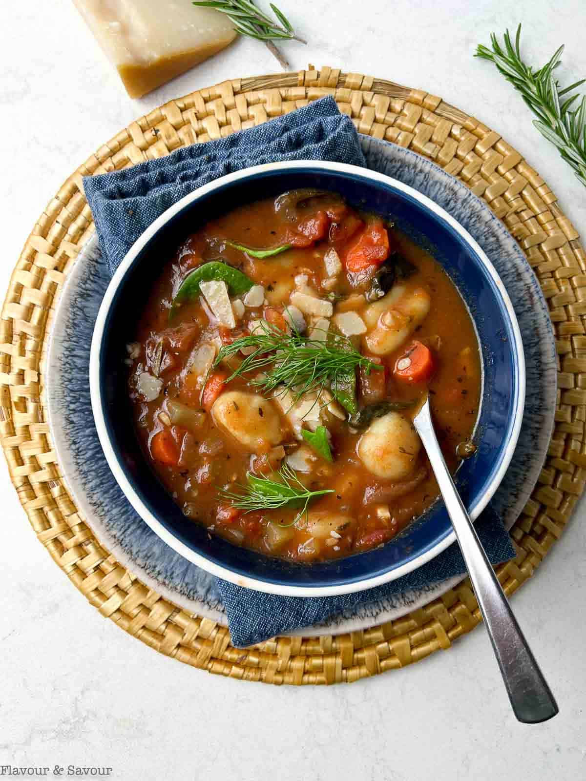 Overhead view of a bowl of Italian vegetable gnocchi soup in a blue bowl with a spoon.