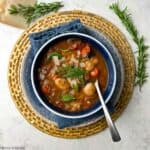 Italian vegetable gnocchi soup in a blue bowl with a spoon.