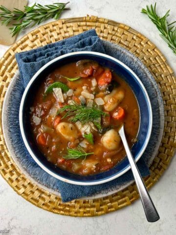 Italian vegetable gnocchi soup in a blue bowl with a spoon.