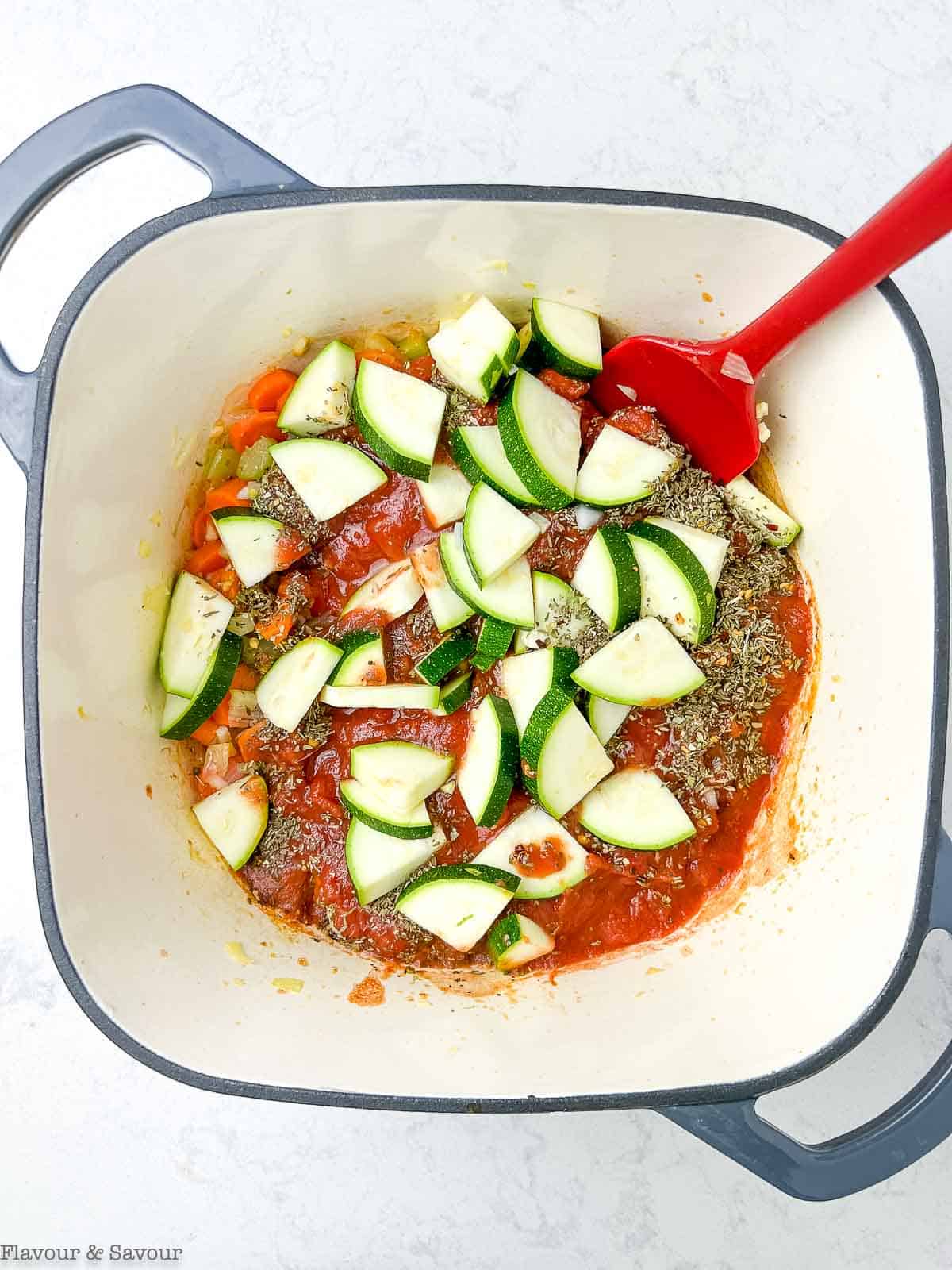 Zucchini, tomatoes and herbs added to a soup pot for gnocchi soup.