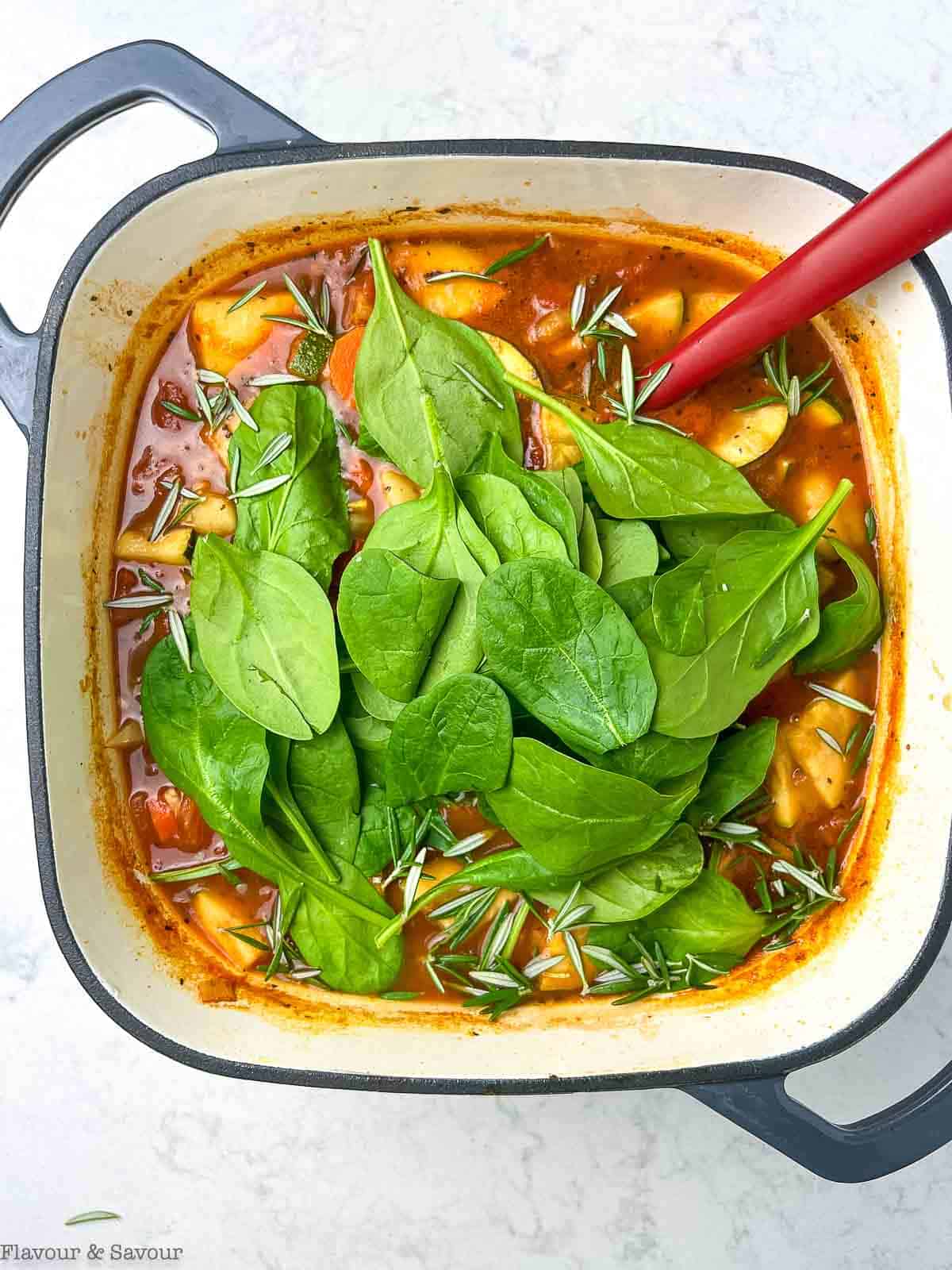 Adding spinach to Italian vegetable gnocchi soup.