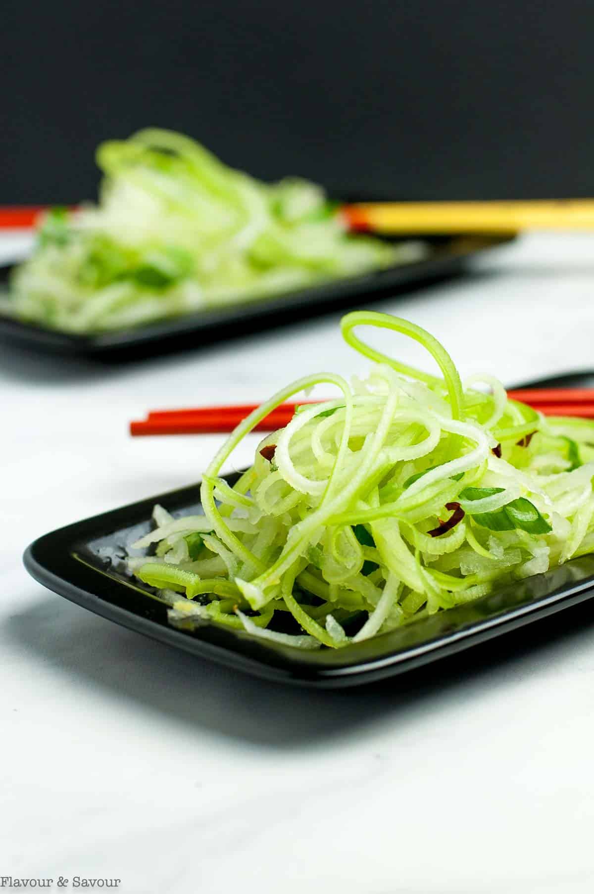 Two small black plates with Asian pear slaw and chopsticks.