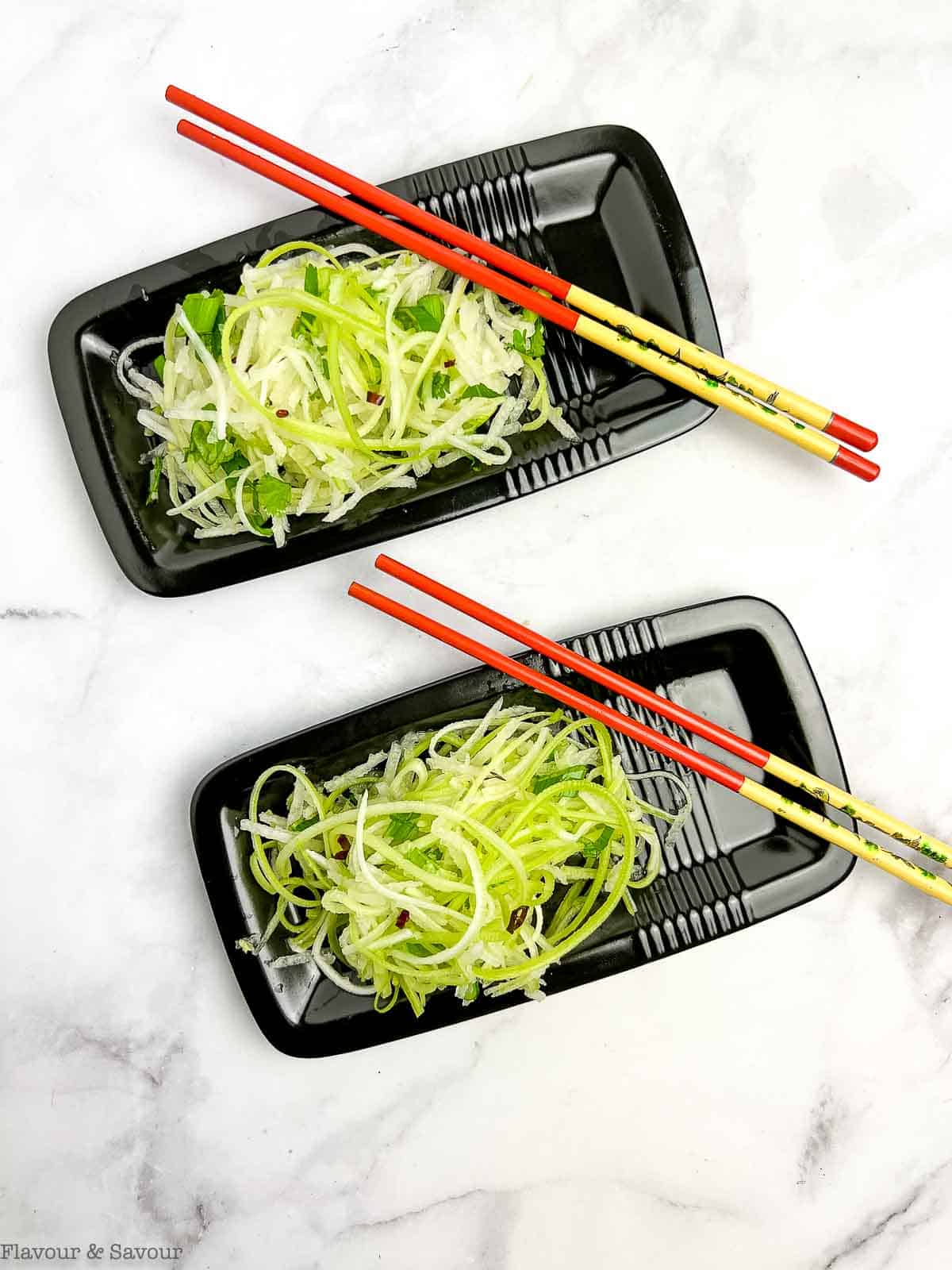 Overhead view of two black rectangular plates each with chopsticks and Asian Pear Slaw.