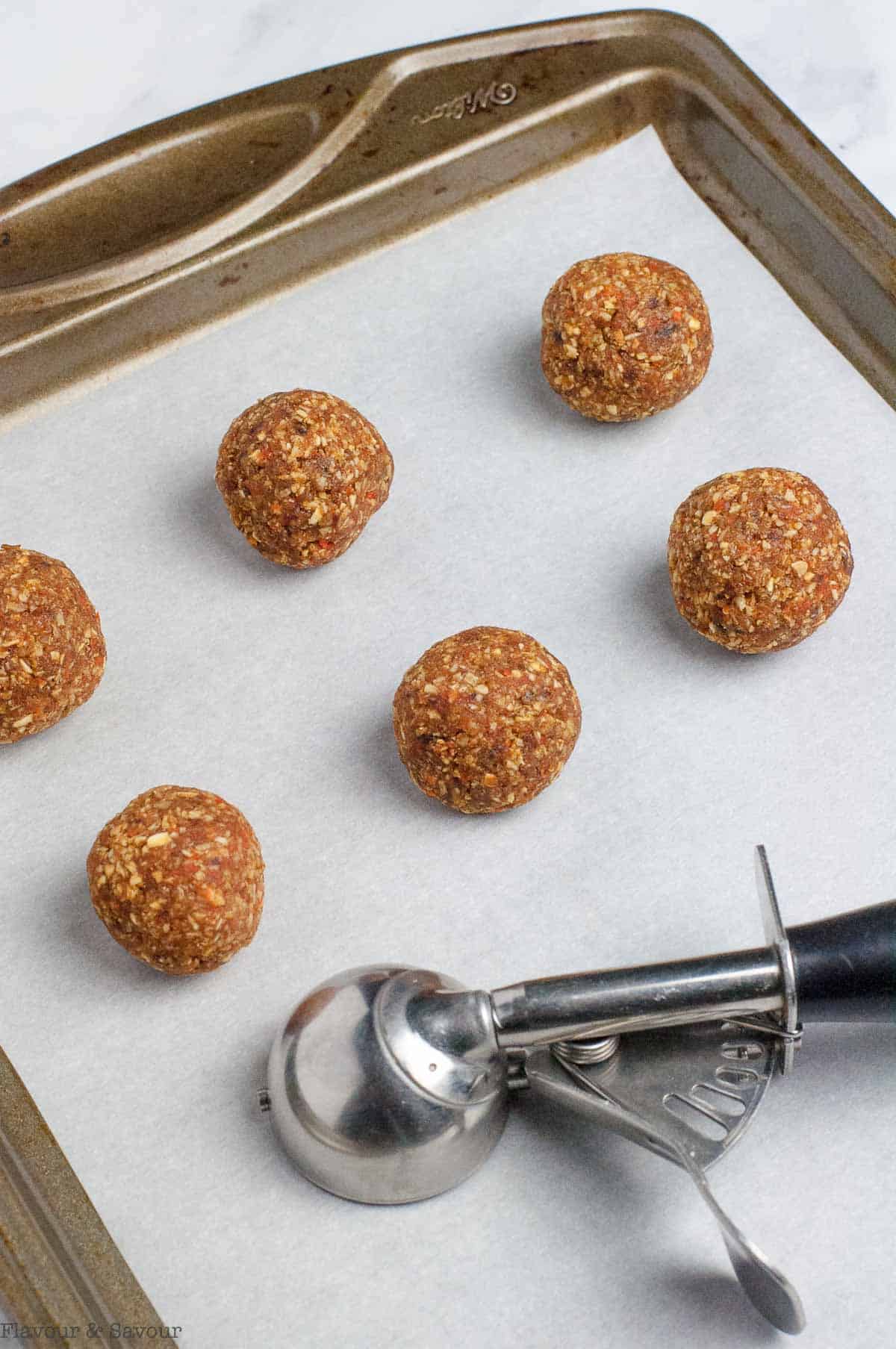 Carrot cake balls on a baking sheet with a small cookie scoop.