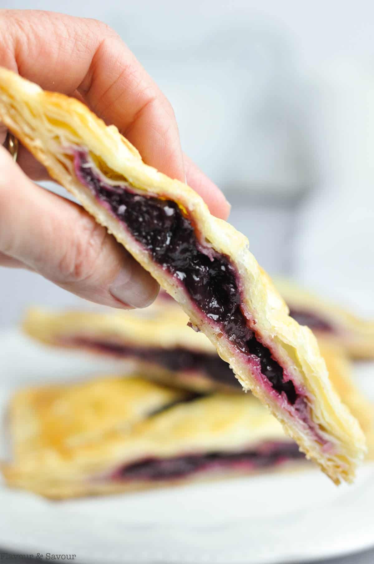A hand holding a gluten-free sliced cherry turnover.
