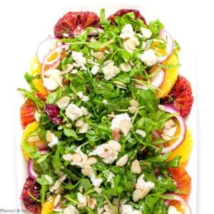 Overhead view of a citrus salad with arugula on a white platter.