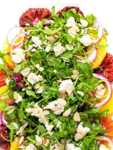 Overhead view of a citrus salad with arugula on a white platter.