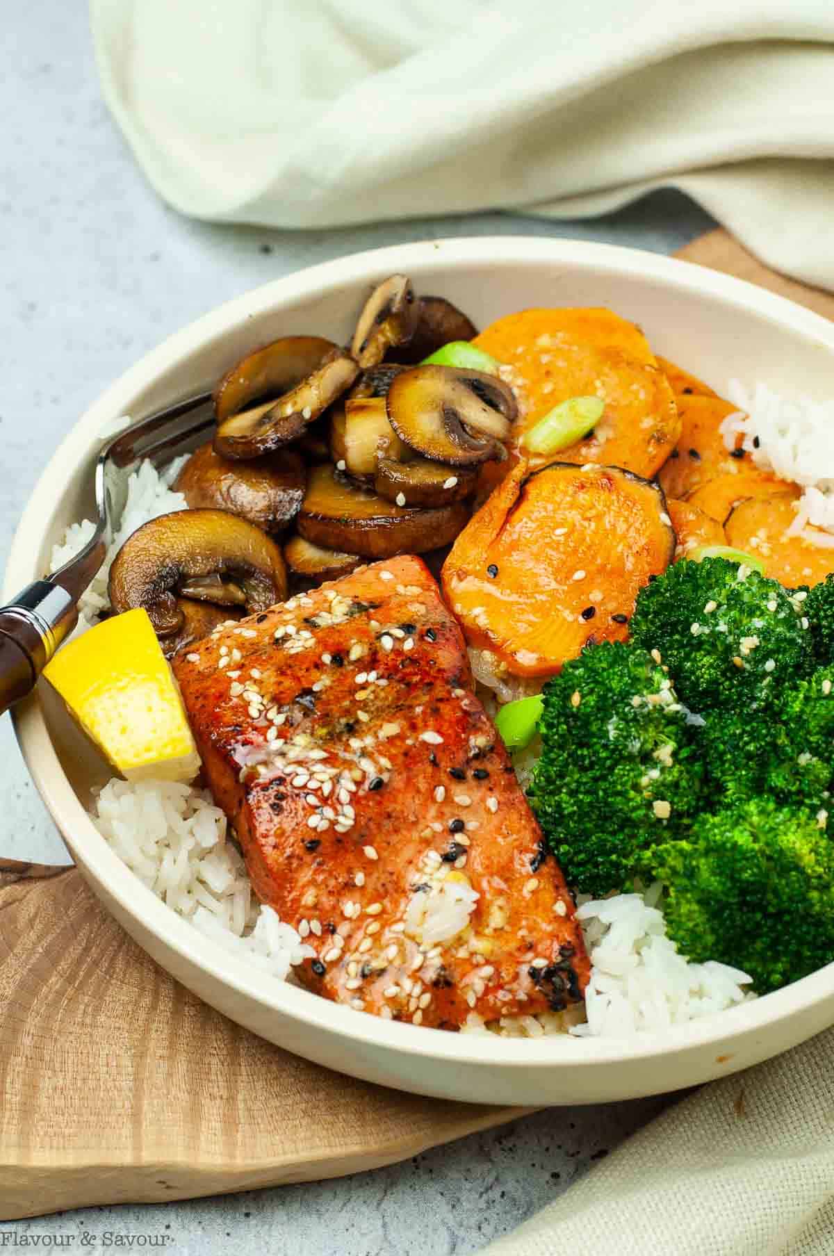 Close-up view of a salmon rice bowl with miso sauce and roasted vegetables.