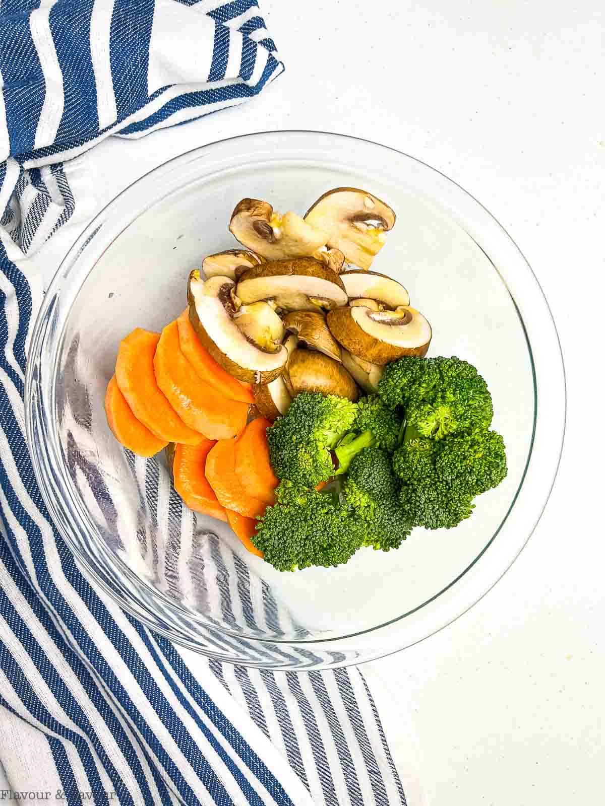 Mushrooms, broccoli and sweet potatoes tossed with olive oil in a glass bowl.