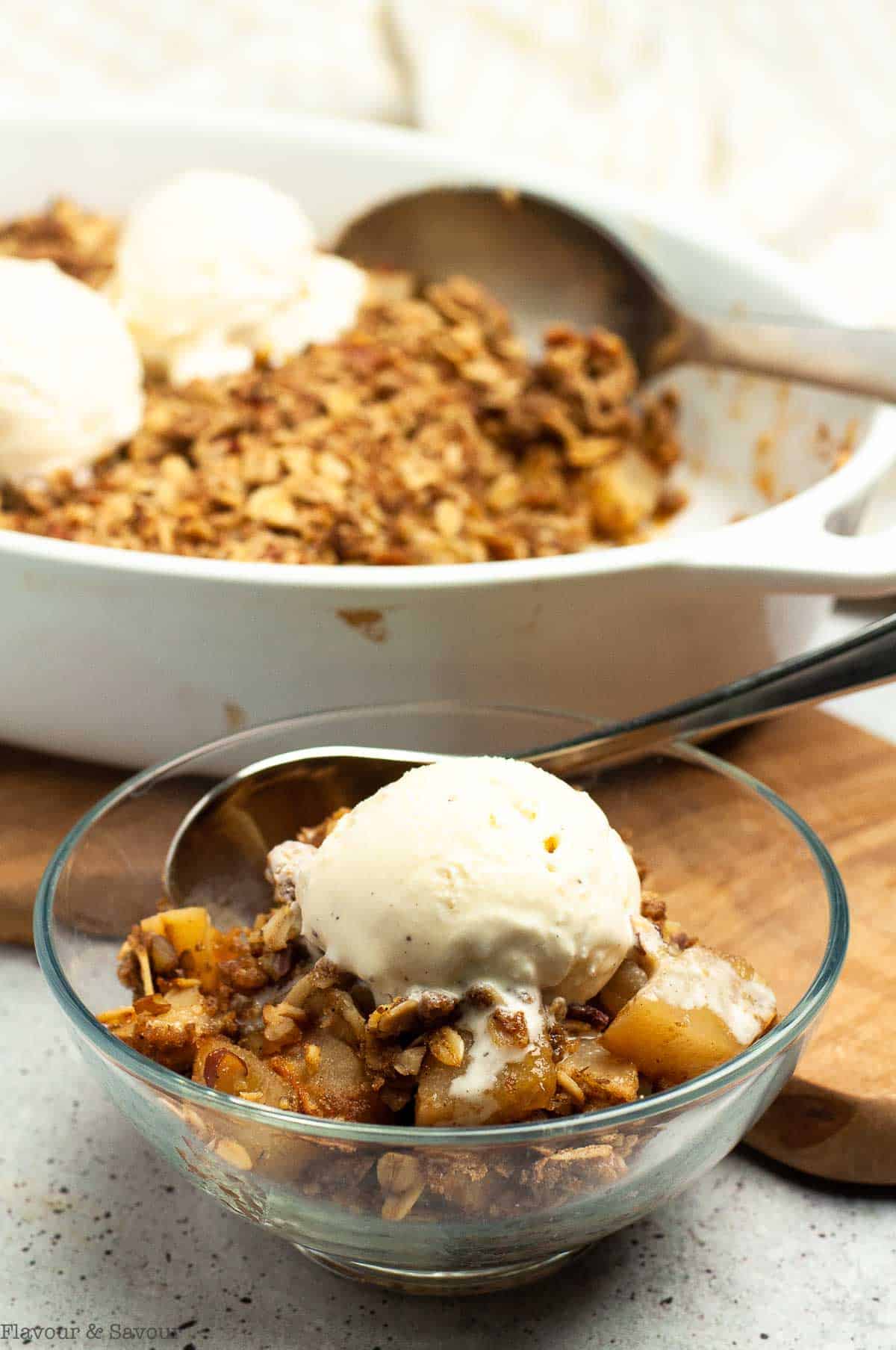 A baking dish and a dessert dish with Pecan Pear Crisp with scoops of ice cream.
