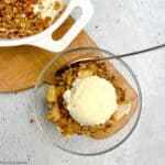 Overhead view of a bowl of pear crisp with pecans and a scoop of ice cream.