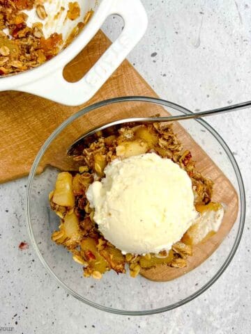 Overhead view of a bowl of pear crisp with pecans and a scoop of ice cream.