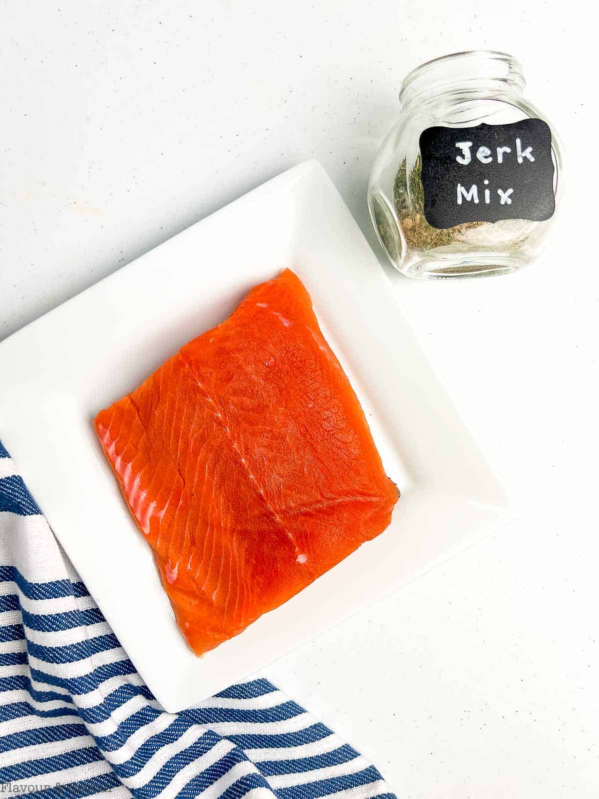 A salmon filet and a spice jar with jerk seasoning.