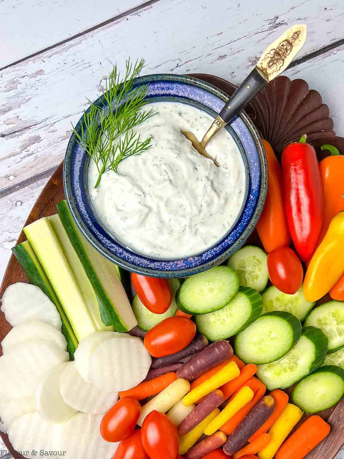 A bowl of creamy Greek yogurt dill dip surrounded by fresh raw vegetables for dipping.