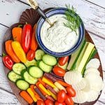 A board with fresh raw vegetables and a bowl of dill dip.