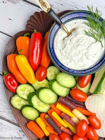 A board with fresh raw vegetables and a bowl of dill dip.