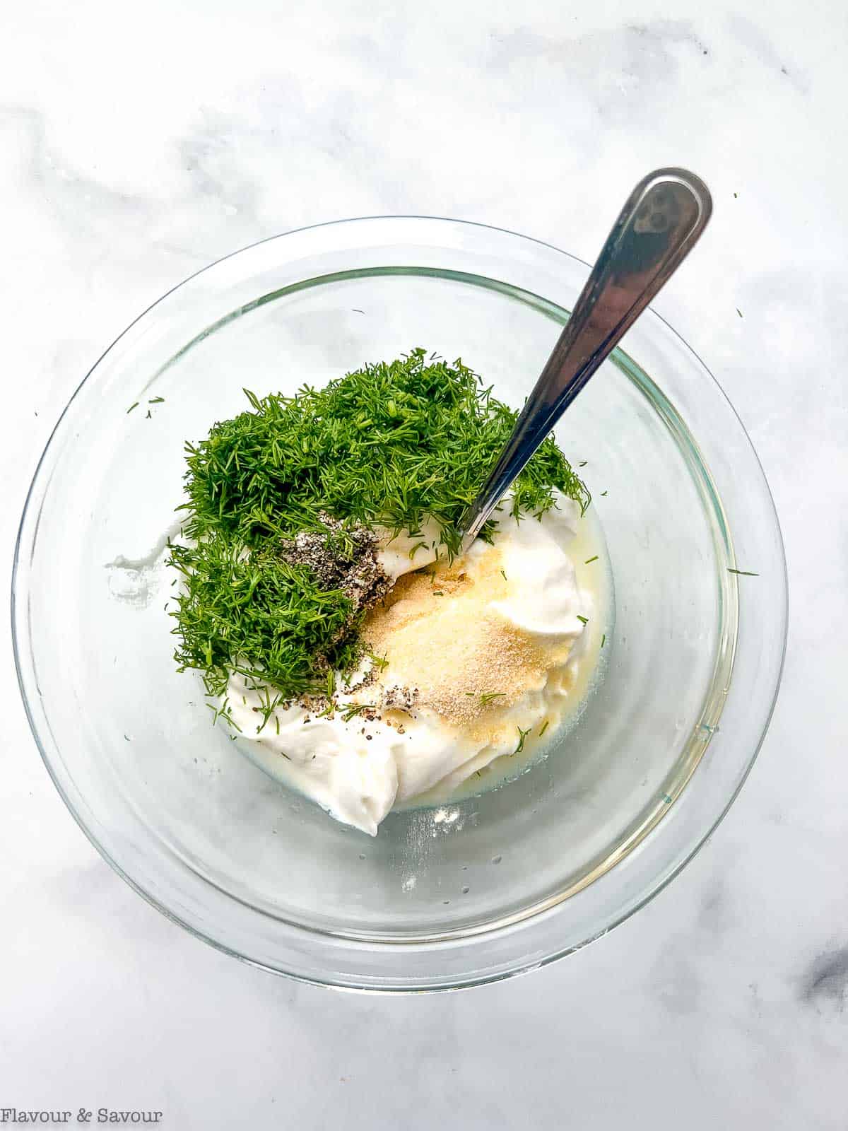 Ingredients for Greek yogurt dill dip in a glass bowl with a spoon.