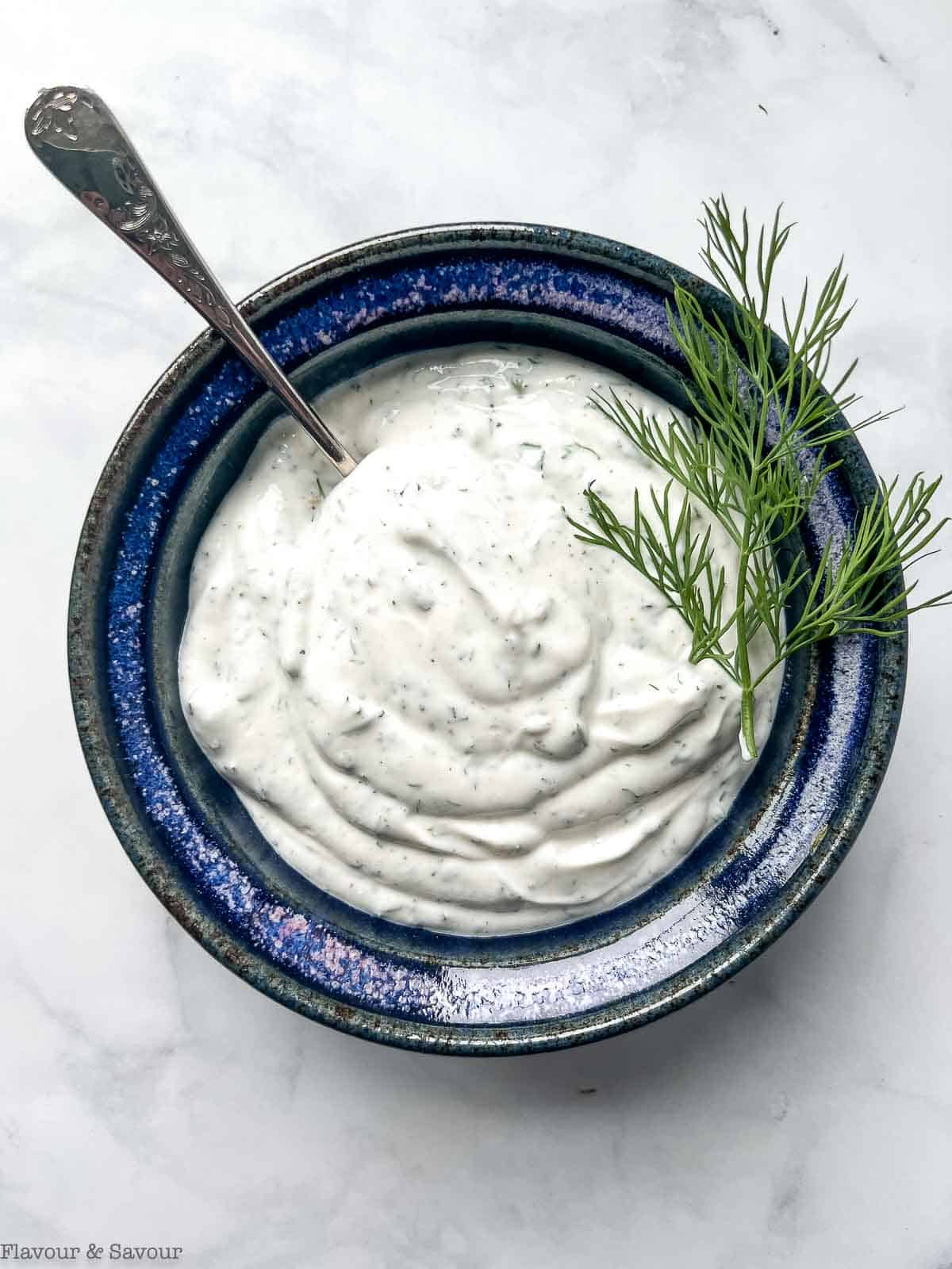 A bowl of Greek yogurt dill dip with a sprig of fresh dill.