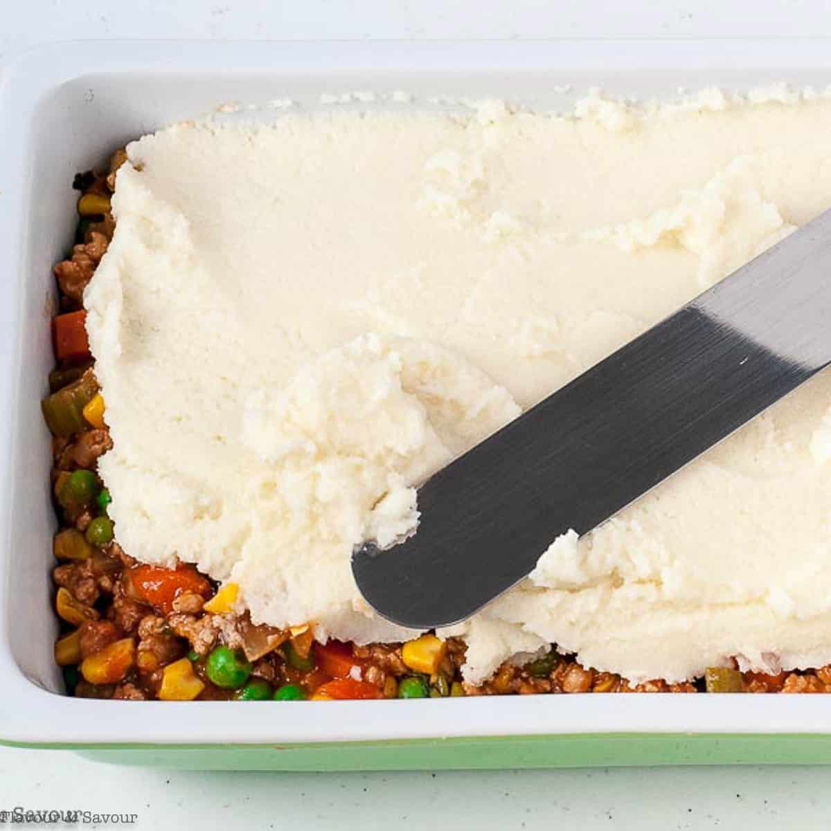 Spreading cauliflower mash over shepherd's pie filling using an offset spatula.