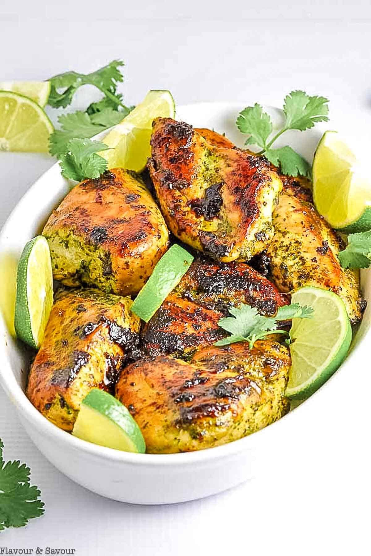 Thai baked chicken breasts in an oval bowl with lime and cilantro sprigs.