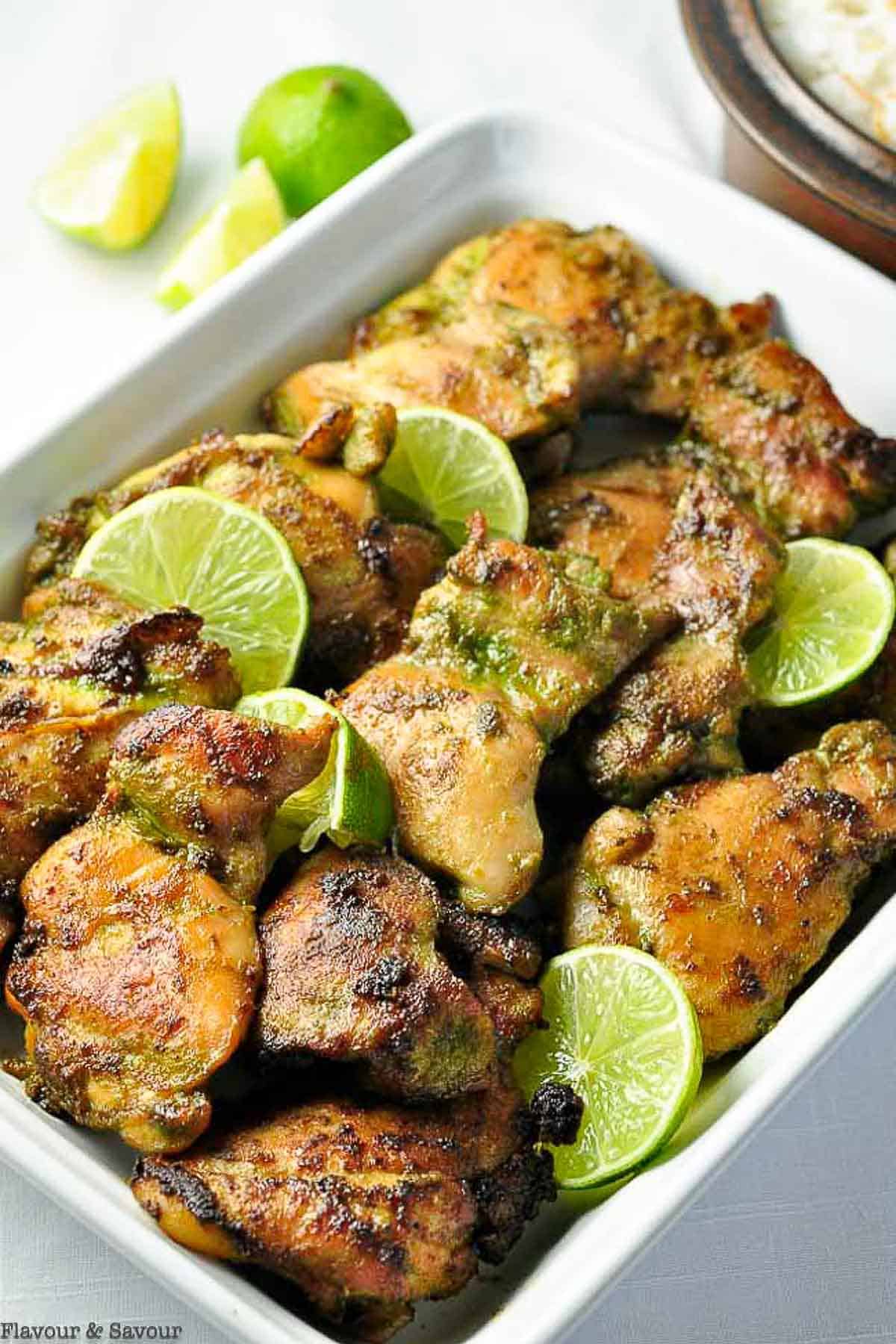 A white serving dish with Thai baked chicken thighs and fresh slices of lime.