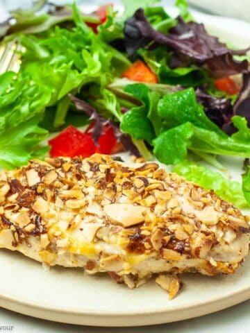 An air-fried almond-crusted chicken breast on a plate with a green salad.