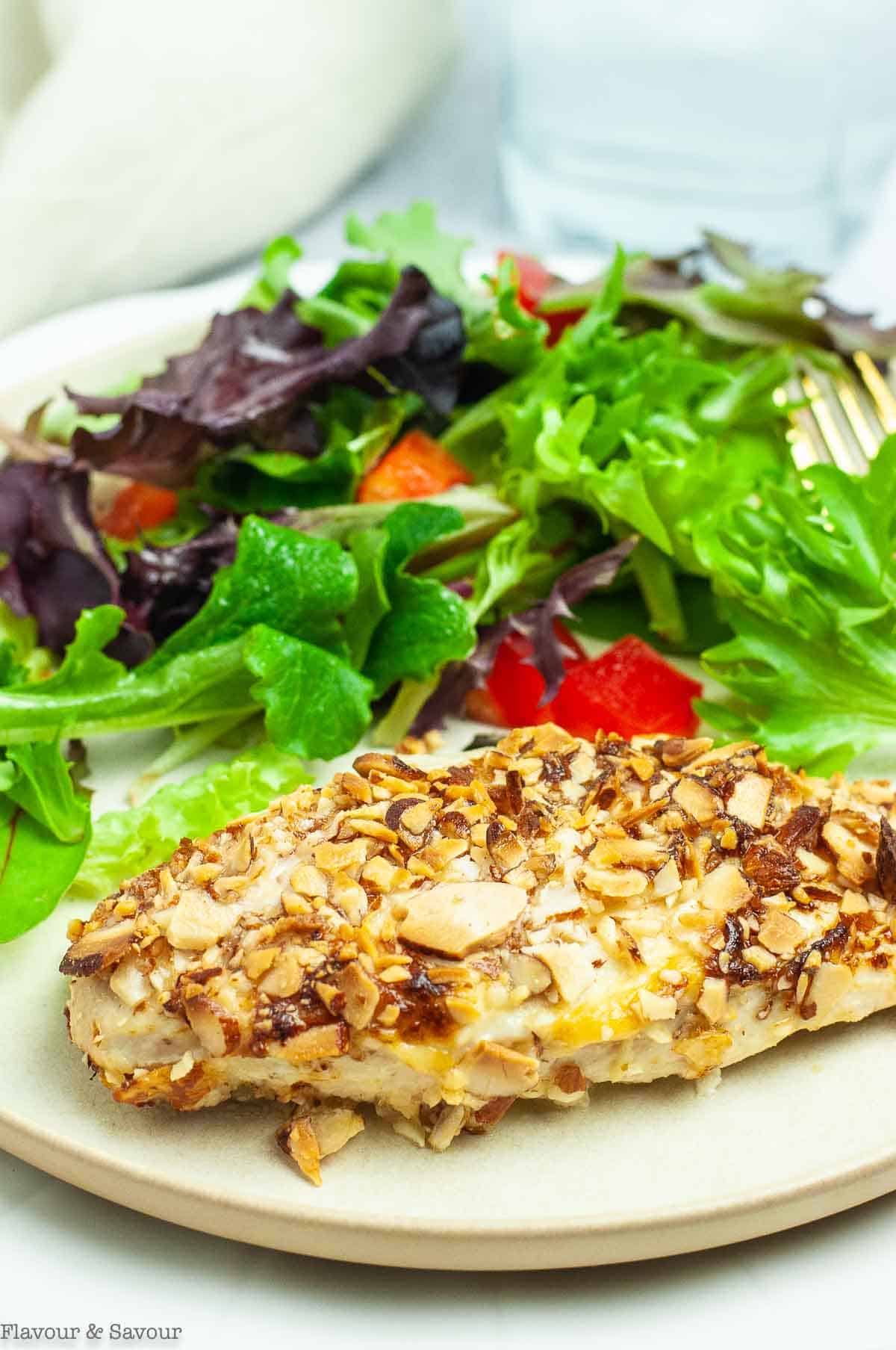 An almond-crusted chicken breast on a plate with a green salad.