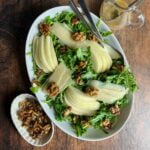 Arugula Pear and Parmesan salad in an oval bowl with a small bowl of maple walnuts beside.