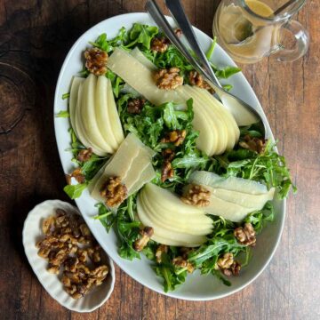 Arugula Pear and Parmesan salad in an oval bowl with a small bowl of maple walnuts beside.