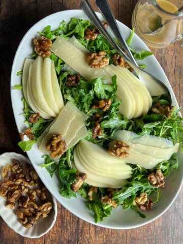 Arugula Pear and Parmesan salad in an oval bowl with a small bowl of maple walnuts beside.