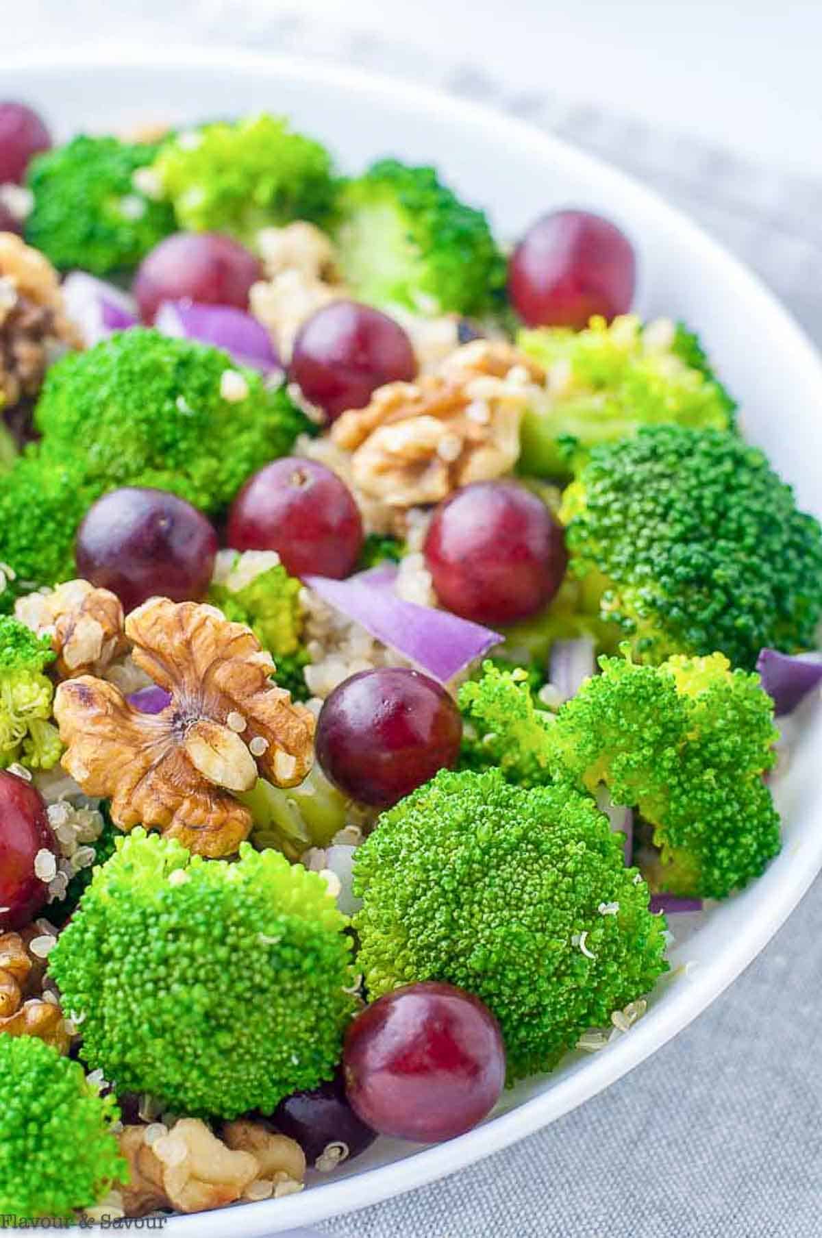Close up view of a bowl of broccoli quinoa salad with red grapes.