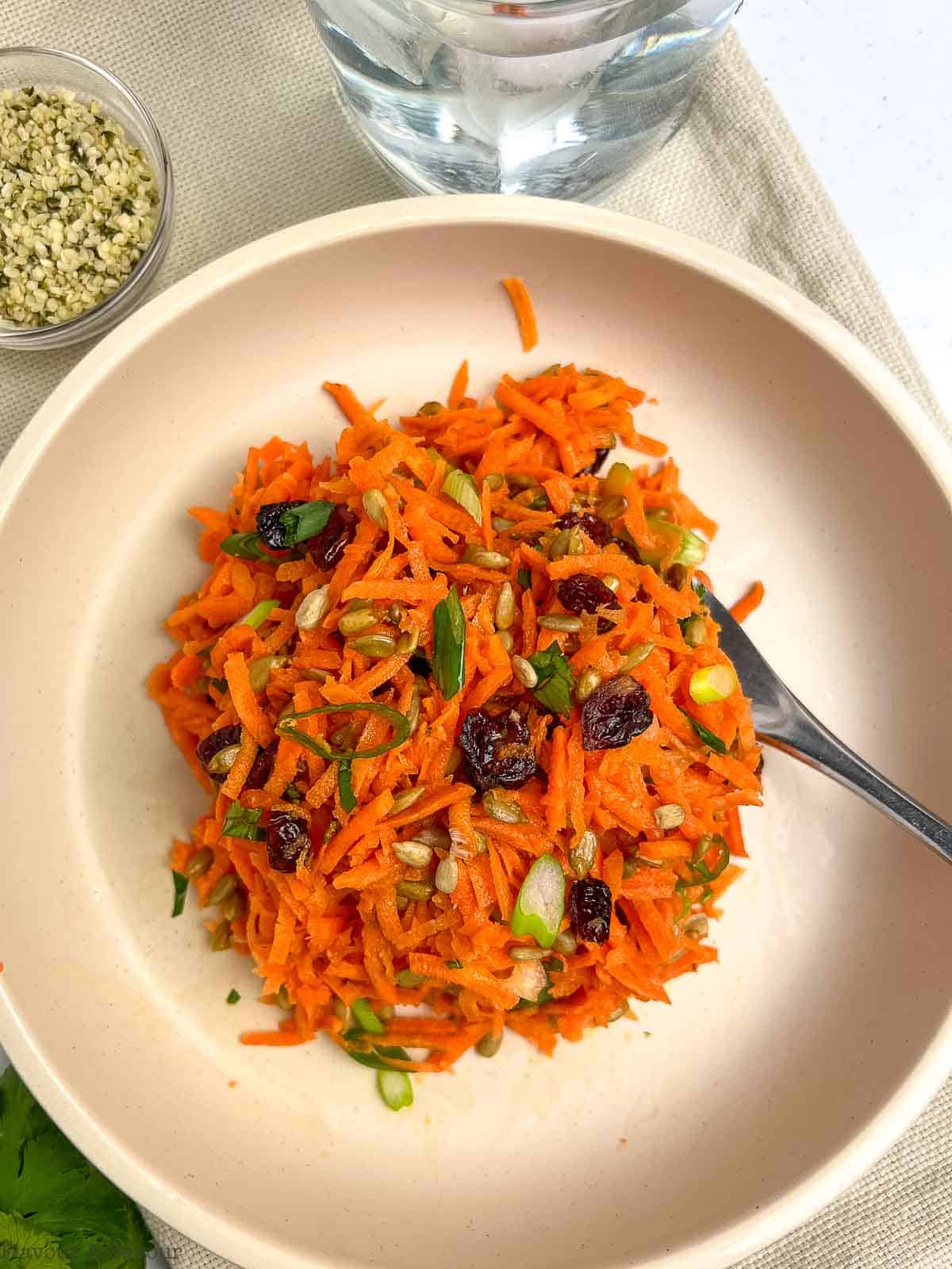 Close up view of carrot salad with cranberries in a bowl with a fork.