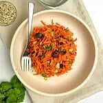 Overhead view of carrot salad with cranberries and sunflower seeds in a shallow bowl.