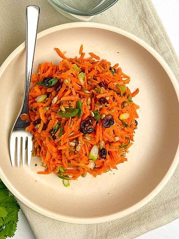 Overhead view of carrot salad with cranberries and sunflower seeds in a shallow bowl.