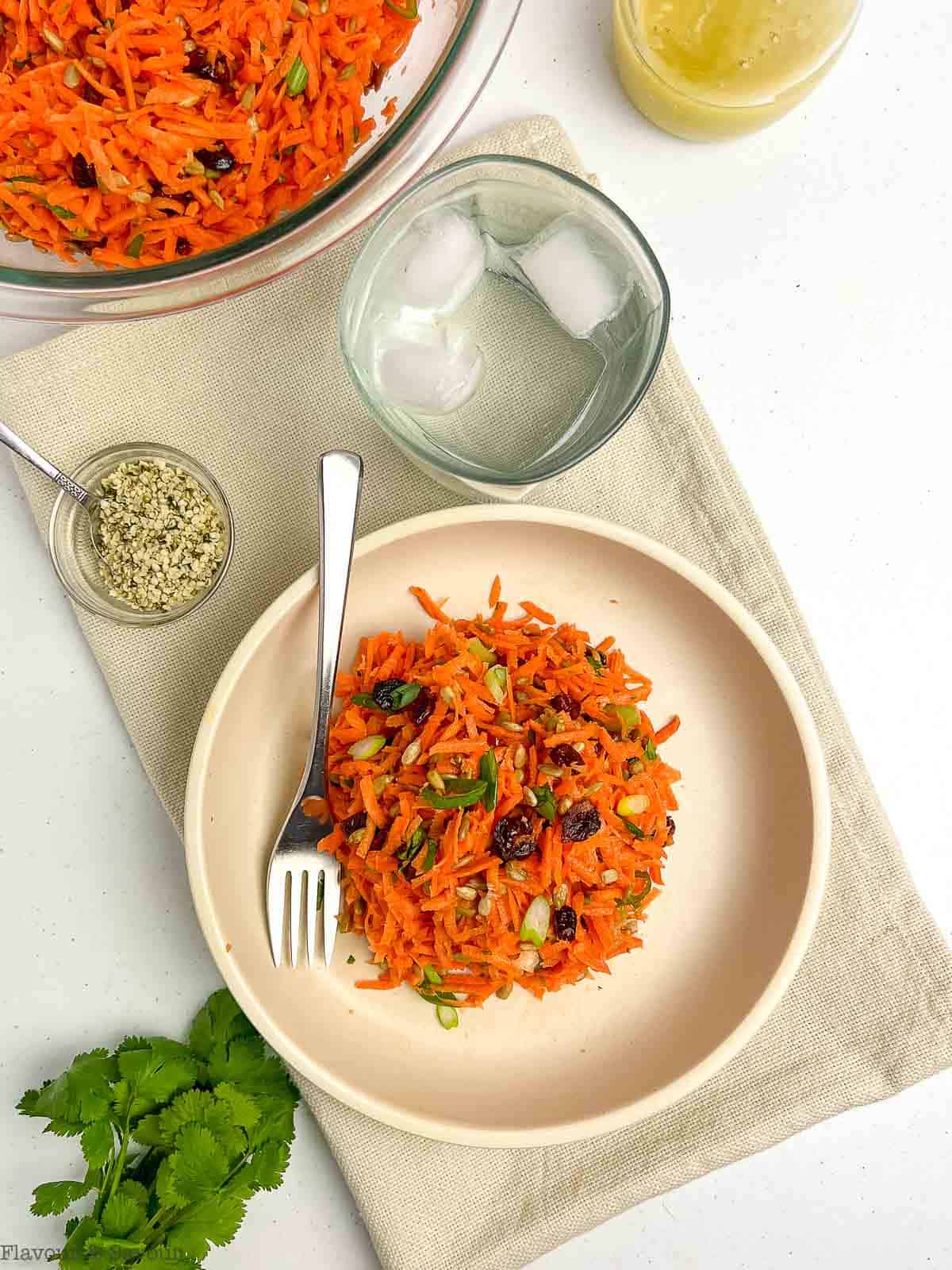 A bowl of carrot salad with cranberries and sunflower seeds with a small dish of hemp hearts beside it.