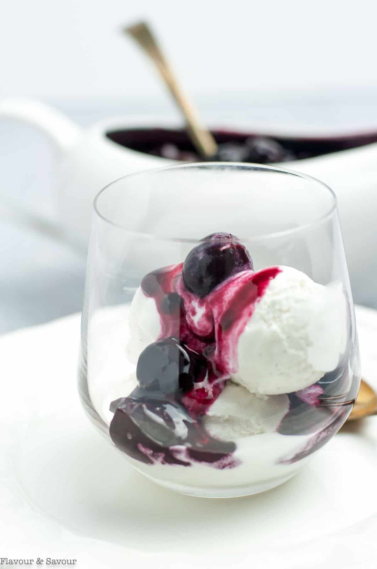 A glass of vanilla ice cream topped with cherry compote or cherry sauce.