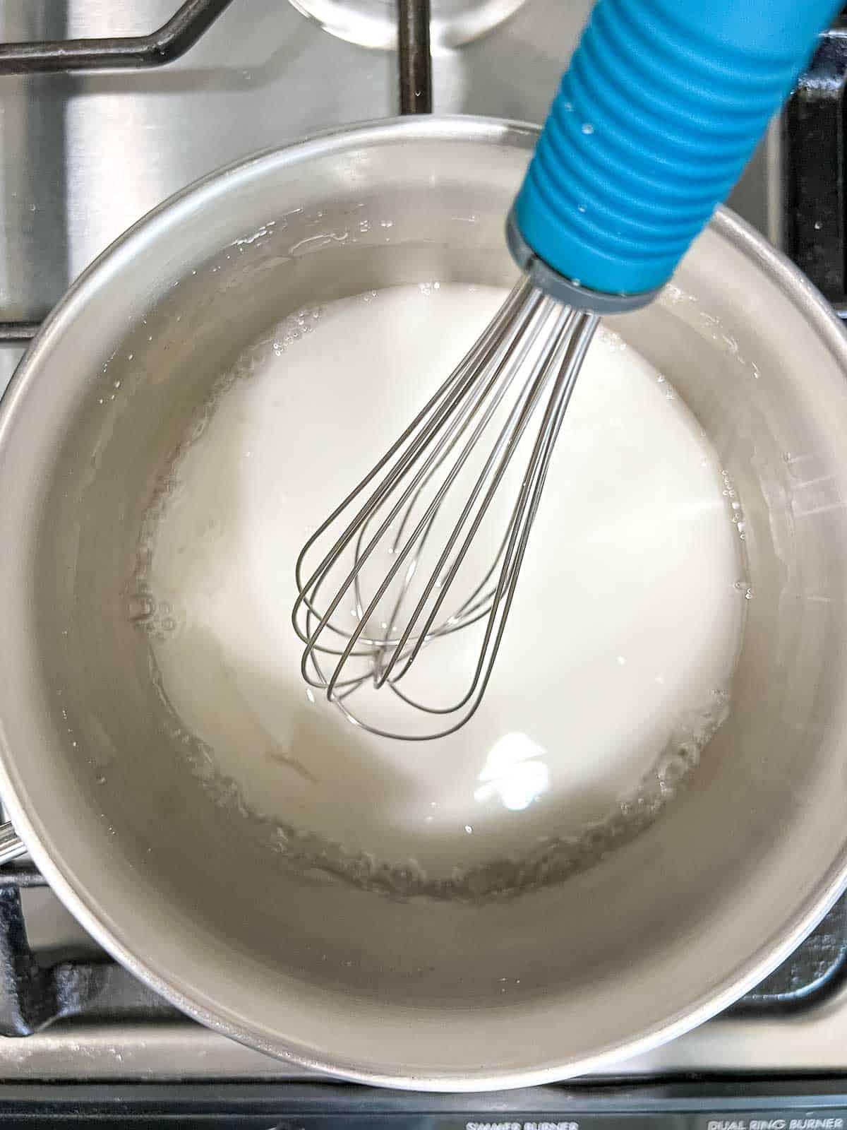 Whisking cornstarch mixture in a saucepan until it thickens slightly.