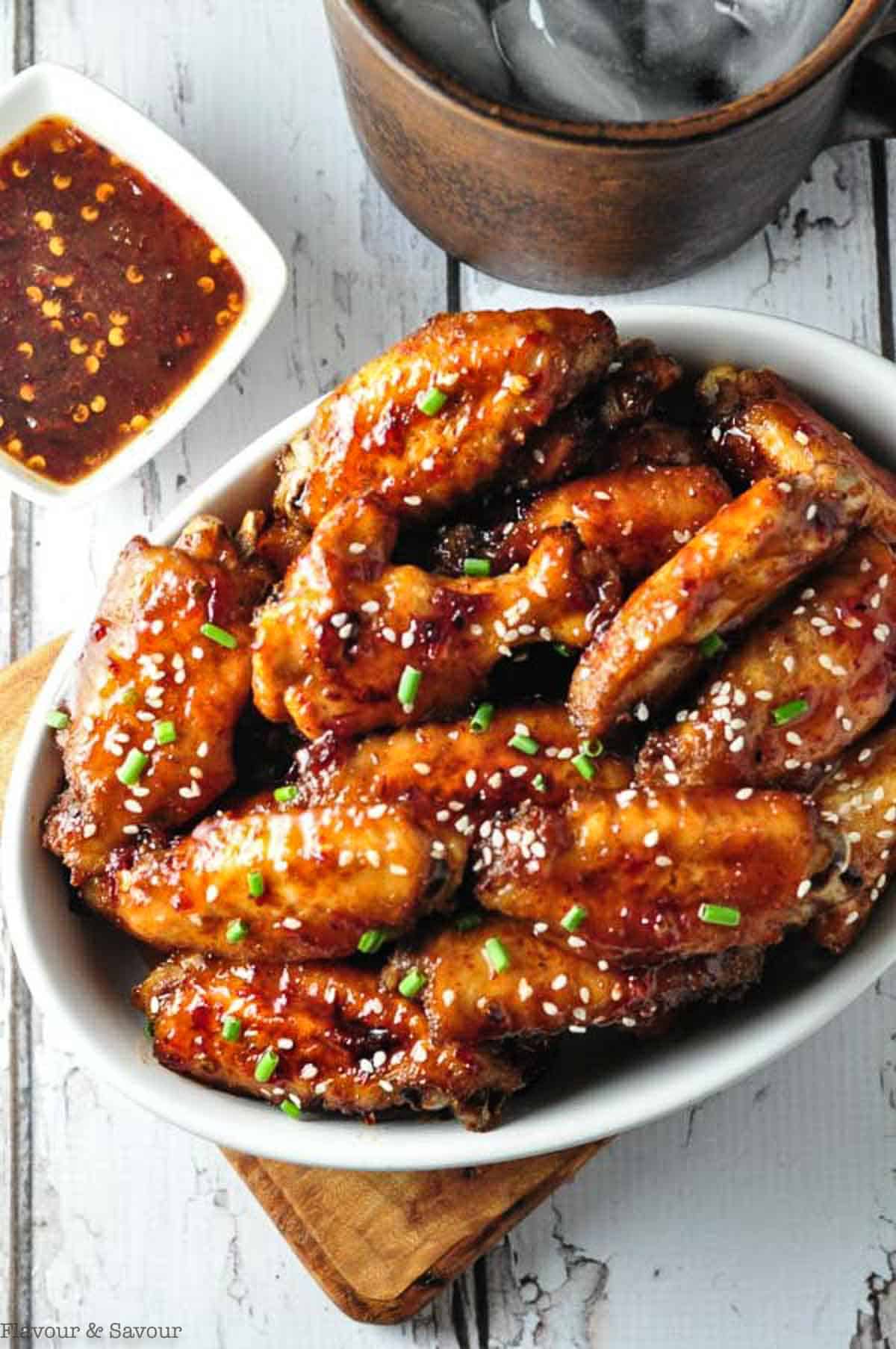 Overhead view of a bowl of chipotle honey-mustard glazed chicken wings garnished with sesame seeds and chives.