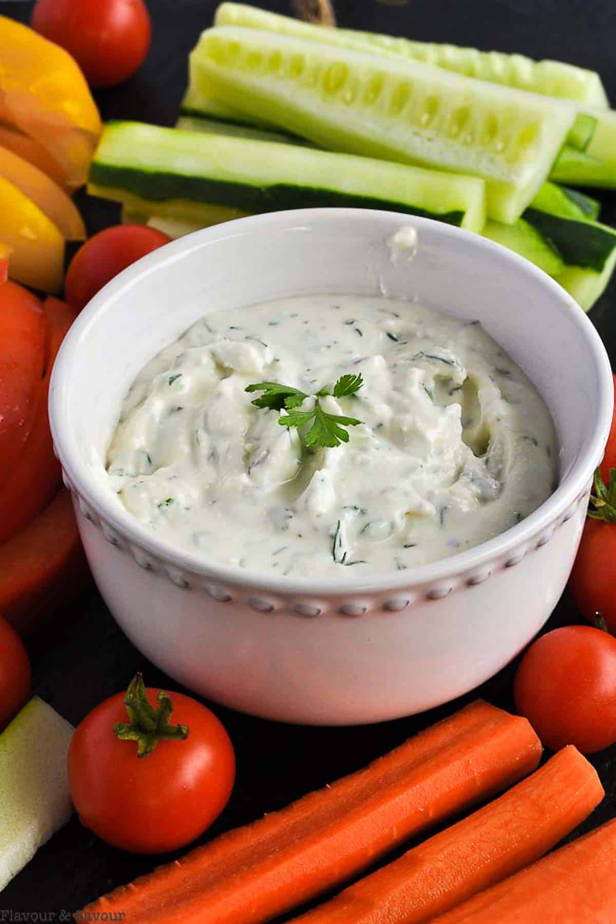 A bowl of feta dip with lemon and herbs surrounded by fresh vegetables.