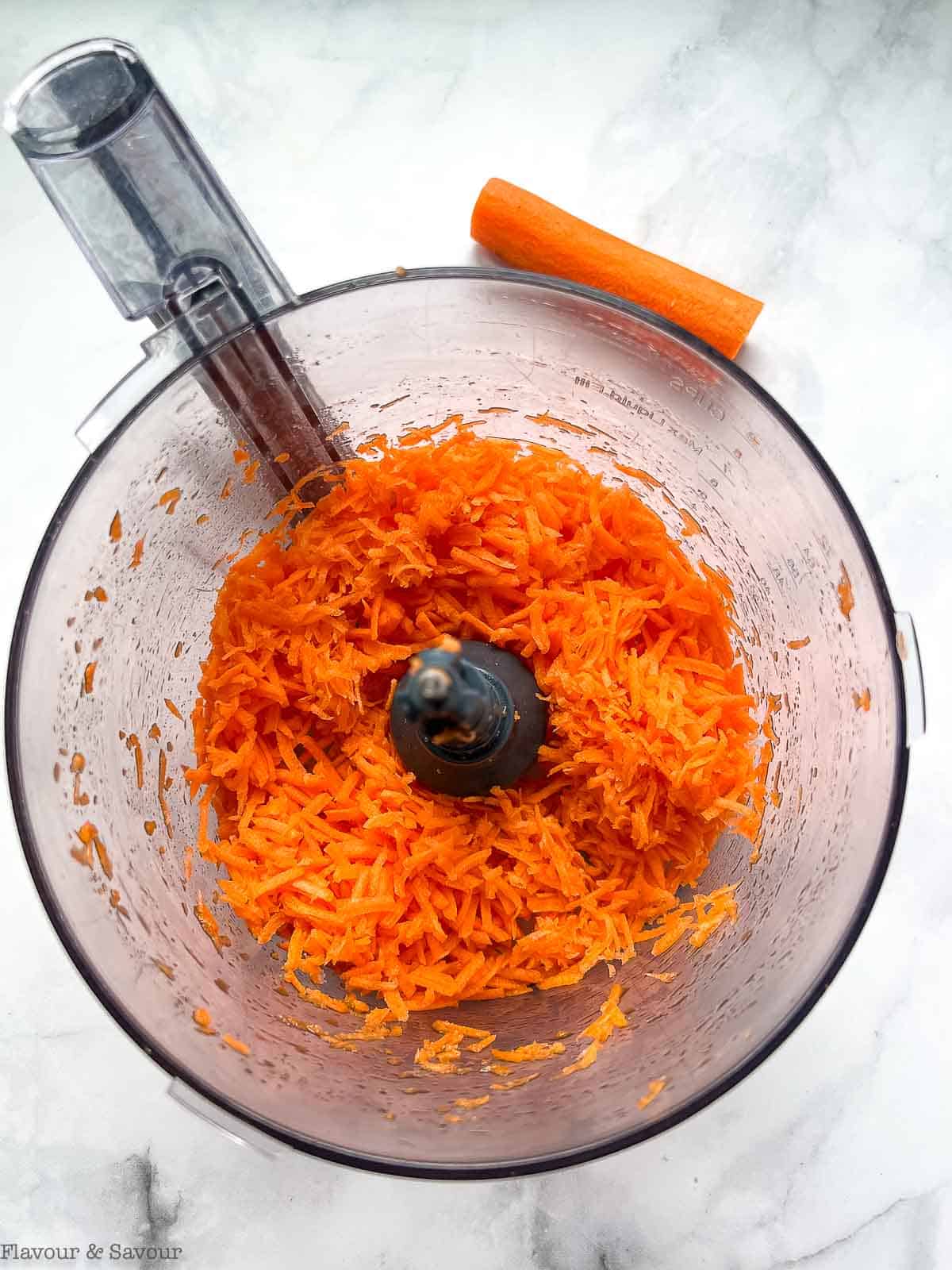 Shredded carrots in the bowl of a food processor.